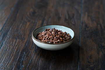 Chocolate Cacao Nibs or Cocoa Nibs in Bowl Ready to Use on Dark Wooden Surface.