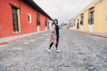 Fototapeta na wymiar Full portrait of Hispanic woman walking in colonial city on a cloudy day - tourist crossing the street in Antigua Guatemala