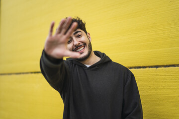 Handsome smiling European skater in a hoodie posing in front of a yellow wall