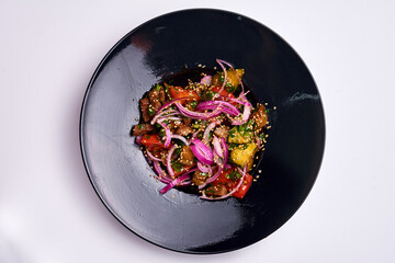 salad of tomatoes, vegetables, onions in a black plate, on an isolate