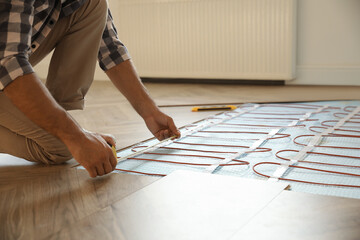 Professional worker installing electric underfloor heating system indoors, closeup