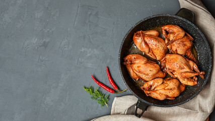 Delicious fried quail carcasses in a frying pan on a dark concrete background. Top view, flat lay....