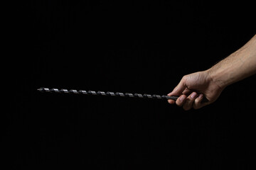 Long drill on a black background. A man's hand holds a long drill. Construction tool