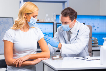 Fototapeta premium Professional doctor makes a coronavirus vaccine using a syringe and hypodermic needle. Professional medical worker and patient at the hospital office. Vaccination and safety.