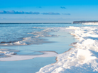 Cold winter sea shore. Pieces of ice by the sea. Blue sky with small clouds