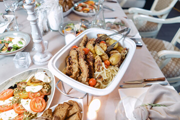 Meat with potatoes and onions, in a white food warmer. Beautiful festive table.
