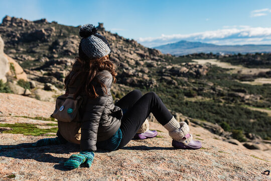 Young active woman with trekking equipment sitting, relaxing and looking at lake and mountains background
