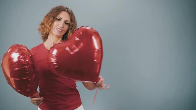 A woman with a red heart in the shape of a balloon smiles on a gray background.