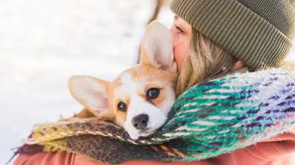 Young happy woman having fun in snowy winter park with Corgi baby dog