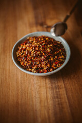 Red chili flakes in a bowl on wooden background. Red cayenne pepper.	