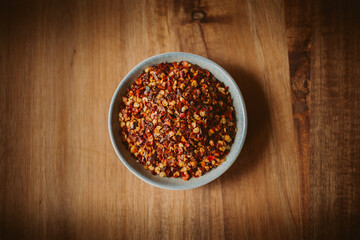 Red chili flakes in a bowl on wooden background. Red cayenne pepper.	