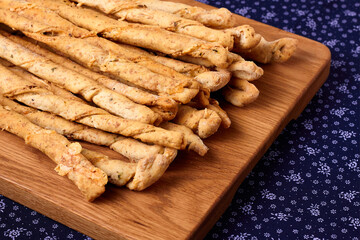 Delicious breadsticks grissini on the wooden board and purple napkin. Italian appetizers.