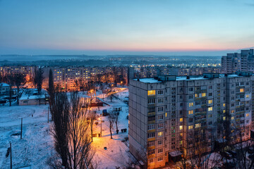 Obraz premium Top view of the evening city in winter with illuminated streets and light in the windows of apartments
