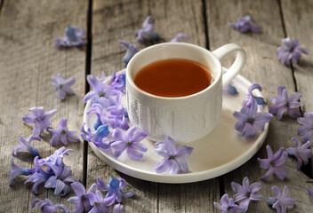  A white cup of tea on a wooden table surrounded by blue flower petals.