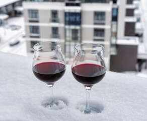 Two glasses of red wine on the snow-covered windowsill of the upper floor of the apartment building.