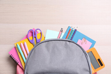 Backpack with different school stationery on wooden table, top view