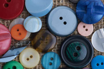 Buttons for clothes are multicolored on a rough jute canvas. Background. Selective focus.