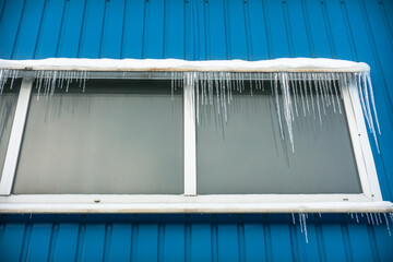 Ice icicles on the metal visor of the window in the house