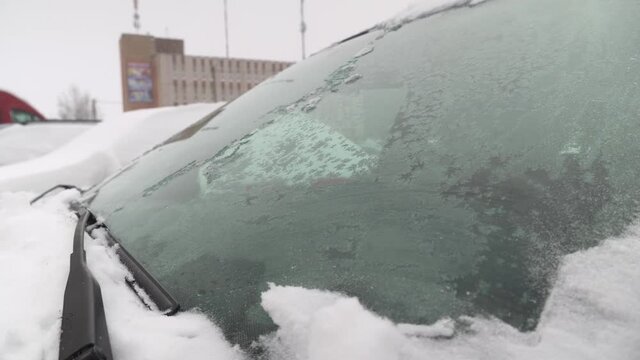 Car windshield brushes slide on frozen snow and ice. Condensate. Poor visibility of the road. Frost on the car window. Weather. Winter blizzard. A woman is sitting in the car. Outside view