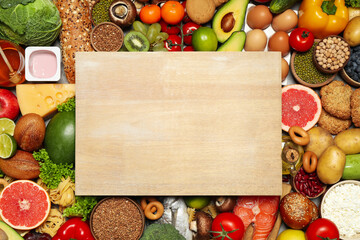 Wooden board on pile of different food products, top view with space for text. Healthy balanced diet