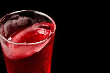 faceted glass with red fruit drink on a black background