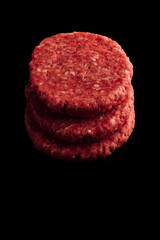 Vertical closeup shot of a stack of raw burger patties on a black surface