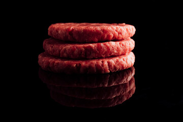 Closeup shot of a stack of raw burger patties on a black surface