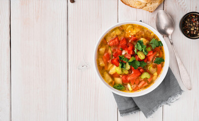 Minestrone soup in white dish on white wooden table, top view. Italian soup with seasonal vegetables. The concept of delicious healthy vegetarian food. Diet idea nutrition. Flat lay with copy space