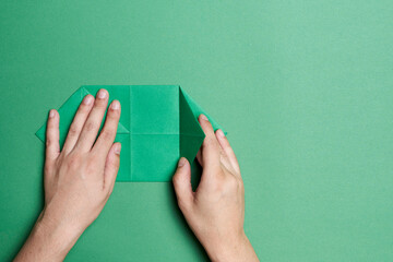 Young hands folding paper to make an origami figure, green paper and background