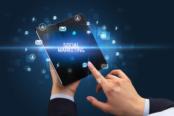 Businessman holding a foldable smartphone with SOCIAL MARKETING inscription, social networking concept