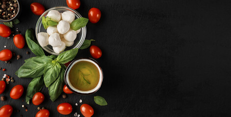 Obraz na płótnie Canvas Mozzarella and cherry tomatoes with basil leaves, salt and pepper, layout on a black stone board. Ingredients for making Caprese salad. Top view with copy space for text