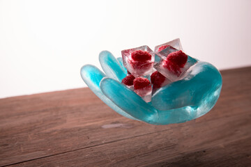 Food art. An ice sculpture in the shape of a hand holds frozen raspberries in ice cubes. Copy space