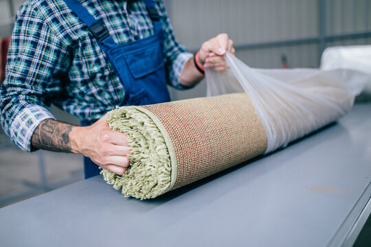 Professional worker packing clean carpet at washing service.
