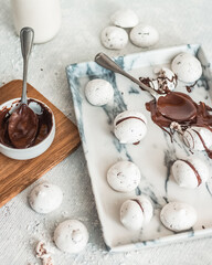 White cookies with chocolate on a tray and a light background, next to a spoon with chocolate, baking process