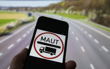 Close up of mobile phone screen with german truck road maut sign, blurred highway background