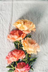 Flat-lay of Beautiful peony flowers over grey linen table cloth background, top view, copy space