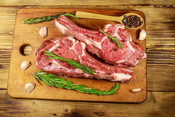 Raw fresh beef rib eye steak on bone with spices, garlic and rosemary on wooden table. Top view