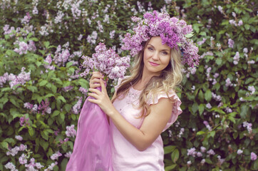 Fototapeta premium Blonde woman enjoying in a spring garden with blooming lilacs with bouquet, lilac flowers hair style. Spring Concept, Spring blossom, Positive human emotions and feelings. 