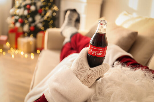 MYKOLAIV, UKRAINE - JANUARY 18, 2021: Santa Claus with Coca-Cola bottle resting on sofa in room, closeup