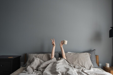 Woman laying in bed, holding mug with coffee in hand and show 