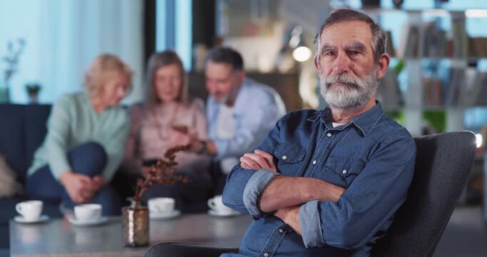Portrait of Caucasian Attractive Pensioner in Blue Jeans Shirt Crossing Arms Smiling to Camera while Spending Weekend with Old Friends. Home Interiors.