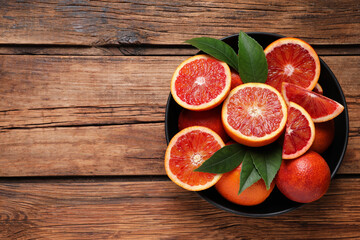 Whole and cut red oranges with green leaves on wooden table, top view. Space for text