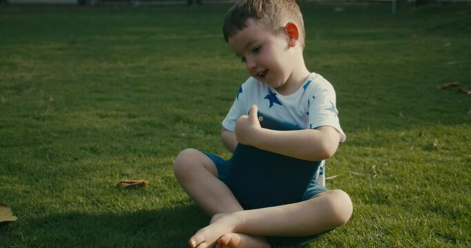 Funny preschooler very happy boy rejoices in victory using digital tablet device,jumping with happiness from victory in a computer game,sitting on the street on grass in park.Kid plays with the tablet