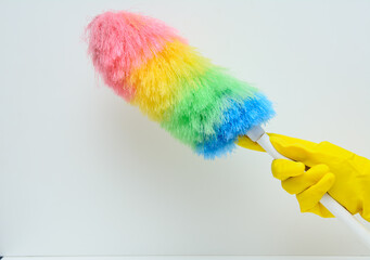 A woman's hand in a yellow rubber glove. There's a feather duster in this hand. White background. Concept-hygiene, maintaining cleanliness