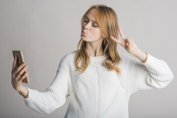 Fototapeta premium Beautiful young girl on a white background in the studio makes a selfie on a smartphone