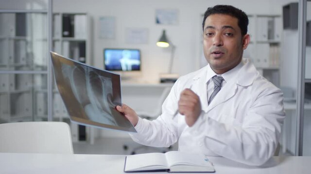Medium portrait shot footage of mature Middle Eastern pulmonologist holding X-ray picture speaking on camera during online meeting