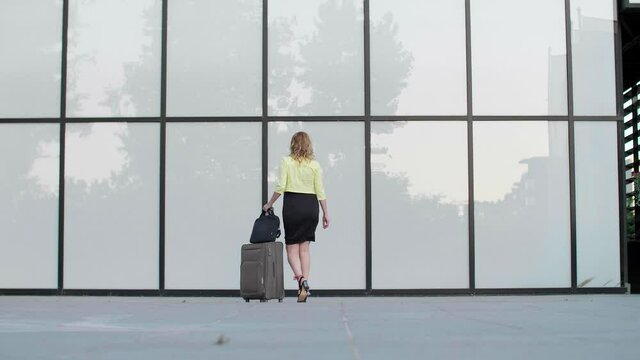 A pregnant woman passing by a modern building with travel luggage