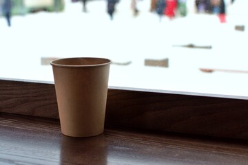 paper cup with coffee on table inside a cafe on blurred background of snowy street