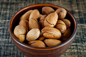 Pecan in a clay bowl on a shabby wooden board. Nuts in shell on an old black table.