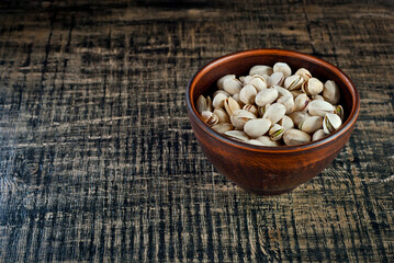 Pistachios in a clay bowl on a shabby wooden board. Nuts in shell on an old black table.  Copy space and free space for text near nuts.